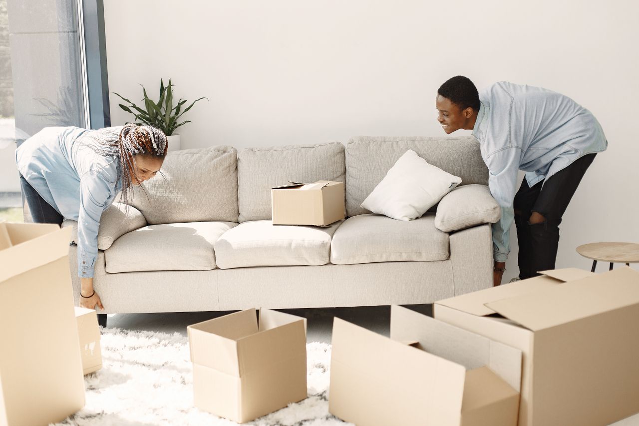 team-01 Joyful couple arranging a sofa in their new home, with moving boxes all around.